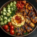 Lemon chili grilled chicken bowls with cucumber salad and hummus on a plate.